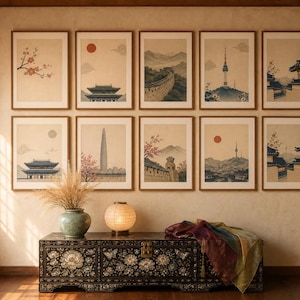 May include: A gallery wall featuring ten framed prints depicting East Asian landscapes and architecture, arranged in two rows above a dark, ornate wooden chest with mother-of-pearl floral inlays, a ceramic vase with dried grass, and a round paper lamp.