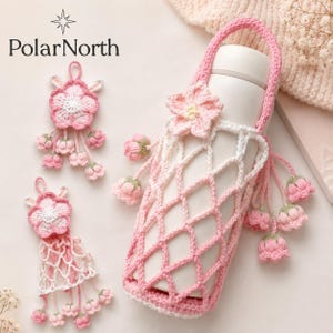May include: A white insulated bottle in a pink and white crochet carrier with a handle. The carrier is decorated with crochet flowers and hanging buds. Two additional crochet flower ornaments are also present. The PolarNorth logo is in the upper left corner.