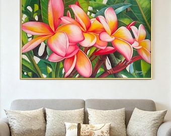 May include: A framed painting of vibrant pink and yellow plumeria flowers with green leaves. The artwork is set against a white wall, above a gray sofa with decorative pillows. The painting has a gold frame.