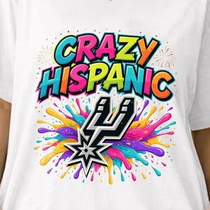May include: White t-shirt with the text "CRAZY HISPANIC" in colorful bubble letters. Below the text is a graphic of a star and a lightning bolt with colorful paint splatter.