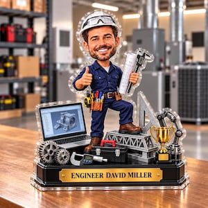 May include: A custom bobblehead figure of an engineer wearing a white hard hat and blue uniform, holding a blueprint and caliper. The base features a laptop, toolbox, gears, a trophy, and a gold plaque reading ENGINEER DAVID MILLER.