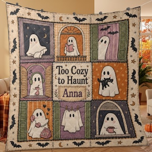 May include: A quilted throw blanket featuring a grid of nine panels with illustrations of ghosts in various activities, including reading, listening to music, and holding a cat. The center panel displays the text Too Cozy to Haunt and the name Anna.