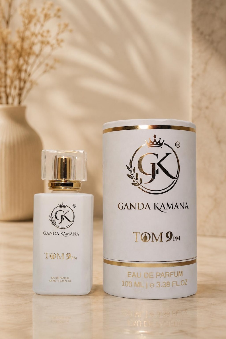 May include: A white rectangular perfume bottle with a clear cap and a matching cylindrical white canister. Both feature a gold logo with the text GANDA KAMANA and TOM 9PM. The label indicates 100 ML and 3.38 FL. OZ. of Eau de Parfum.