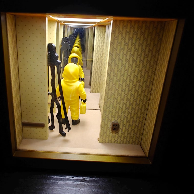 Może przedstawiać: Diorama przedstawiająca postać w ż&oacute;łtym kombinezonie trzymającą ż&oacute;łty kanister w korytarzu z ż&oacute;łtą tapetą we wzory. Po lewej stronie stoi wysoka, cienka czarna postać. Lustra na obu końcach tworzą efekt nieskończonego odbicia.