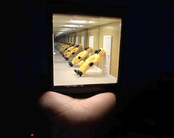 Może przedstawiać: Miniaturowe pudełko diorama z efektem nieskończonego lustra, tworzące powtarzający się obraz postaci w żółtym kombinezonie ochronnym opierającej się o białe drzwi. Wewnętrzne ściany są w kolorze jasnobrązowym z subtelnym wzorem i oświetlone.
