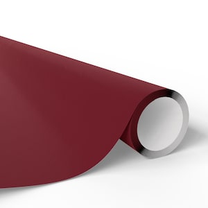 May include: A roll of deep red paper with a silver metallic edge. The paper is a solid colour and appears smooth. The roll is partially unrolled, revealing the white interior.