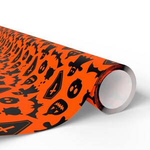 Puede incluir: Un rollo de papel de regalo naranja con un patrón negro repetido con temática de Halloween. El patrón incluye murciélagos, fantasmas, ataúdes y calabazas. El papel está enrollado, mostrando el patrón en el exterior.