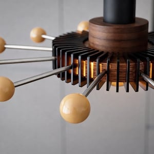 May include: Contemporary chandelier with a black and wood finish. The light fitting has a circular design with metal rods, each with a beige sphere. The centre has a layered wood and black cylindrical structure.