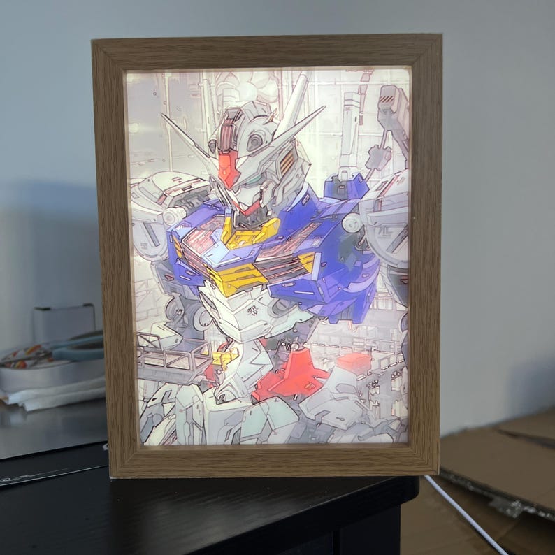 Puede incluir: Ilustraci&oacute;n enmarcada de un robot con una combinaci&oacute;n de colores azul, rojo, amarillo y blanco. El robot est&aacute; representado en una pose din&aacute;mica, con componentes mec&aacute;nicos detallados. El marco es de madera marr&oacute;n claro y la imagen est&aacute; iluminada desde atr&aacute;s.