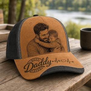 May include: A brown and black baseball cap featuring a detailed image of a father and child embracing. The cap's brim displays the words "Best Daddy Ever" with a heartbeat line design. The cap is made of a soft material.