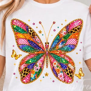 May include: A white short-sleeve t-shirt featuring a large, colorful butterfly graphic on the front. The butterfly wings are decorated with various patterns including leopard print, floral motifs, and glittery textures in shades of pink, orange, and blue.