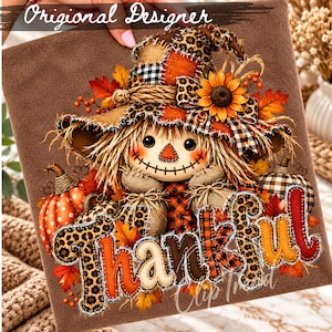 May include: A brown fabric square featuring a scarecrow with a patchwork hat, sunflower, and pumpkins. The word Thankful is printed in large, textured letters with leopard print, plaid, and orange patterns, surrounded by autumn leaves.