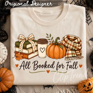 May include: A cream-colored t-shirt featuring a graphic of a stack of books with a bow, a coffee cup with a heart, a pumpkin, and a plaid scarf. The text "All Booked for Fall" is printed below the graphic in a black cursive font with small hearts.