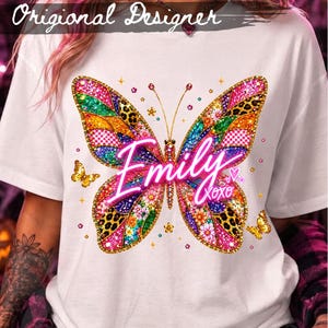 May include: A white t-shirt featuring a large, colourful butterfly graphic with a mix of leopard print, floral, and glitter-style patterns in pink, gold, and green. The name Emily is printed in a bright pink script across the centre with XOXO.