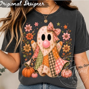 Puede incluir: Una camiseta gris carbón con un gráfico central de un fantasma hecho de varios parches de tela estampada, que lleva un lazo floral y sopla una burbuja rosa. El fantasma está rodeado de flores coloridas, estrellas y dos calabazas naranjas.