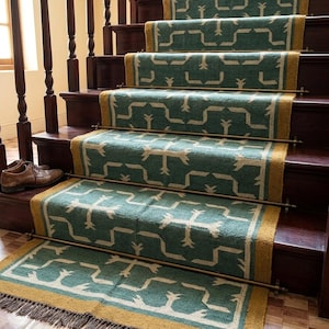 May include: A teal and mustard yellow stair runner with a geometric pattern, secured by brass stair rods on dark wooden steps. The runner features a fringed edge at the bottom and a repeating white linear design across the teal fabric surface.
