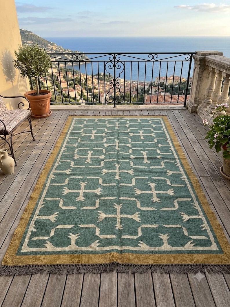 May include: A rectangular area rug featuring a teal green field with a repeating white geometric pattern of crosses and interlocking lines. The rug is bordered by a solid mustard yellow band and finished with short gray fringe on both ends.