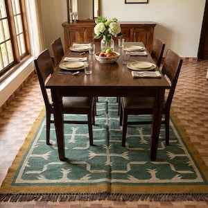 May include: A rectangular area rug featuring a teal green base with a cream-colored geometric pattern and a mustard yellow border. The rug has a fringed edge and is positioned underneath a dark brown wooden dining table with matching chairs.