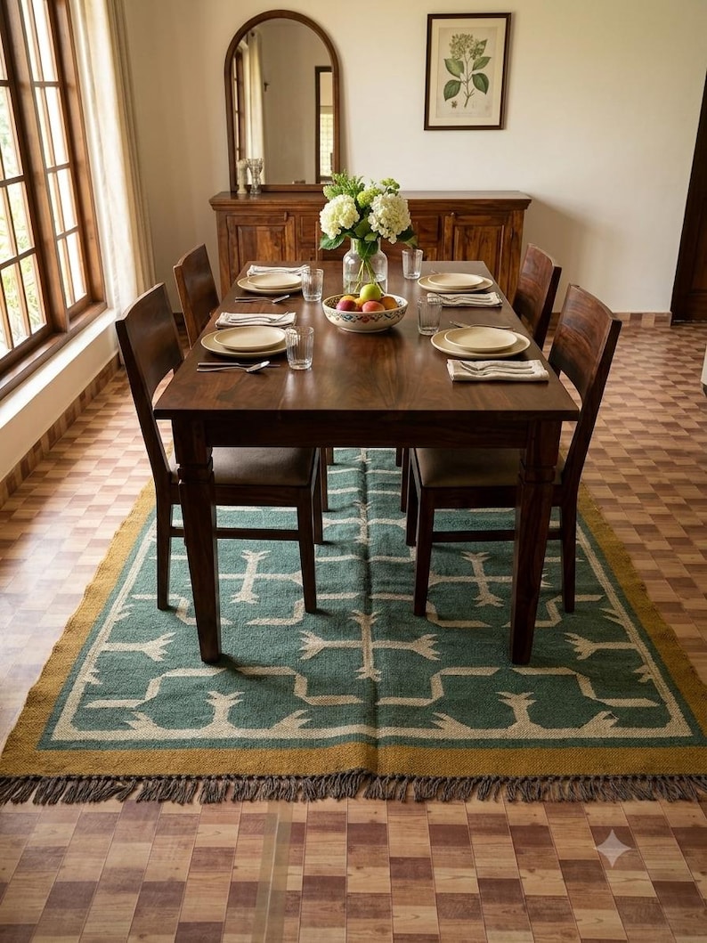 May include: A rectangular area rug featuring a teal green base with a cream-colored geometric pattern and a mustard yellow border. The rug has a fringed edge and is positioned underneath a dark brown wooden dining table with matching chairs.