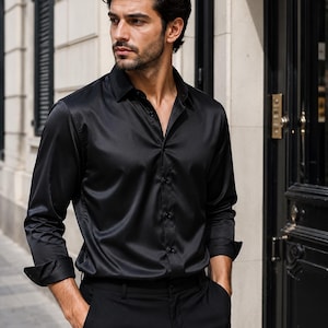 May include: A long-sleeved black button-down shirt with a pointed collar and a smooth, slightly reflective finish. The shirt features a front button placket, cuffed sleeves, and a tailored fit, paired with matching black trousers.