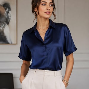 May include: A navy blue short-sleeved button-down shirt with a satin finish, featuring a classic collar and cuffed sleeves, paired with high-waisted cream-colored trousers that have front pleats and a button closure at the waistband.