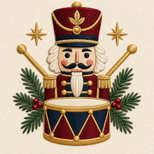 Könnte beinhalten: Eine Stickerei eines Nussknackers in einer rot-blauen Uniform mit Goldverzierungen, der eine Trommel spielt. Das Motiv umfasst zwei gekreuzte Trommelstöcke, grüne Tannenzweige, rote Beeren und zwei goldene Sterne auf cremefarbenem Stoff.