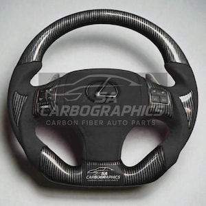 May include: A black and carbon fibre steering wheel with the Lexus logo in the centre. The wheel has integrated controls and the text "SA Carbographics Carbon Fiber Auto Parts". The wheel has a textured grip.