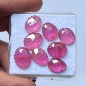 May include: Eight oval-cut pink gemstones are presented in a clear plastic case. The gems have multiple facets, creating a sparkling effect. The container has a white base, enhancing the gems' colour.