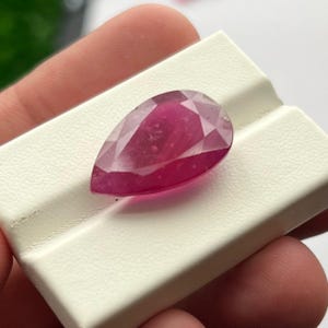 Op de afbeelding: Een gefacetteerde, peervormige robijn edelsteen. De edelsteen is diep, levendig rood met interne insluitsels, tegen een witte achtergrond. De slijping van de steen onthult meerdere facetten, waardoor de glans wordt versterkt.