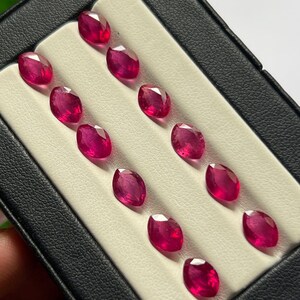 Könnte beinhalten: Eine Sammlung von zwölf facettierten Rubinen im Marquise-Schliff, die in zwei parallelen Reihen in einem schwarzen Etui mit weißem Samteinsatz angeordnet sind. Jeder Edelstein zeigt eine tiefe, leuchtend rote Farbe mit klaren Oberflächen.