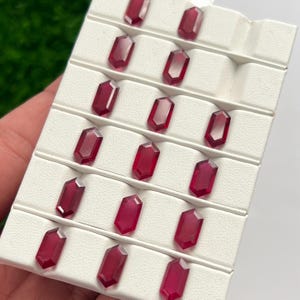 Peut inclure: Une collection de quatorze pierres précieuses en vrac, de couleur rouge profond et de taille hexagonale, disposées dans un plateau de présentation blanc avec des fentes individuelles. Chaque pierre présente une surface facettée.