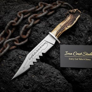 May include: A custom knife with a serrated blade and a handle made of antler. The blade has an etched design. A business card with the text "Iron Crest Studio" and "Every Cut Tells A Story" is next to the knife. A rusty chain is in the background.