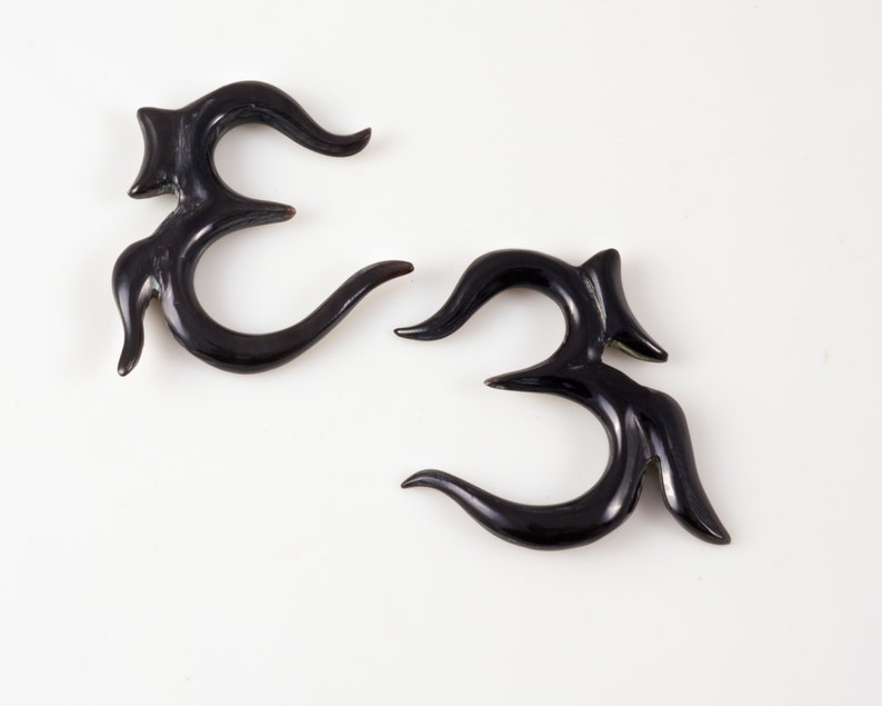 K&ouml;nnte beinhalten: Zwei schwarze Horn-Ohrenstrecker in Form des Om-Symbols.
