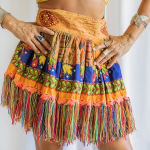May include: A colorful, multi-layered skirt with a fringe hem. The skirt is made of cotton and has a variety of patterns and colors, including orange, blue, green, and red. The skirt is also decorated with small beads and sequins.