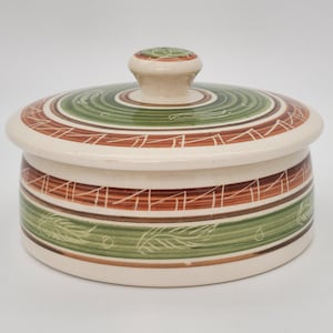 May include: A ceramic lidded jar with a cream base and lid. The lid has concentric rings of green and brown, with a small knob. The jar's body has horizontal bands of green and brown with leaf designs.