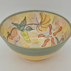 May include: A ceramic bowl with a yellow interior featuring hand-painted floral motifs in green, orange, and yellow. The exterior has a solid yellow base with a wide sage green band around the upper rim. The interior surface has a mottled texture.