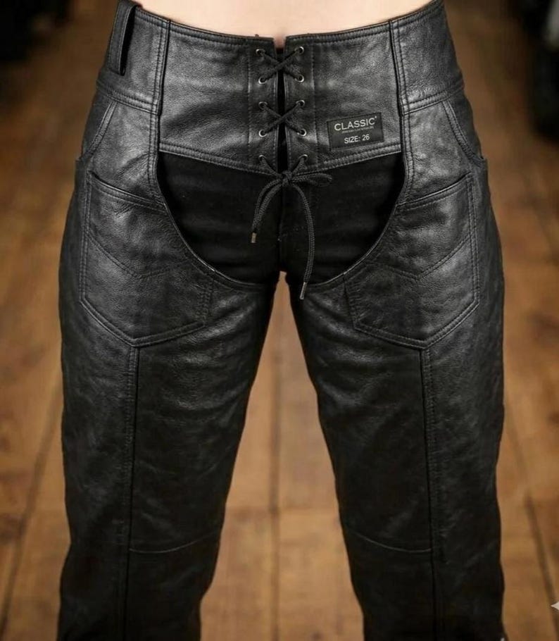 May include: Black leather pants with a lace-up front and a high waist. The pants have a classic design with pockets and a size 26 label. The leather appears textured and worn.