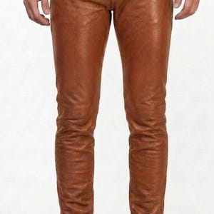 May include: Brown leather trousers with a matching belt and buckle. The trousers are worn with black boots. The leather trousers have a classic, fitted design. The belt is brown with a gold buckle.