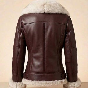 K&ouml;nnte beinhalten: Eine dunkelbraune Lederjacke mit einem dicken, cremefarbenen Kunstfellkragen sowie passendem Kunstfellbesatz an den &Auml;rmelb&uuml;ndchen und am Saum. Die Jacke verf&uuml;gt &uuml;ber vertikale Nahtdetails auf der R&uuml;ckseite und verstellbare Seitenschnallen an der Taille.