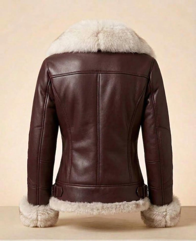 K&ouml;nnte beinhalten: Eine dunkelbraune Lederjacke mit einem dicken, cremefarbenen Kunstfellkragen sowie passendem Kunstfellbesatz an den &Auml;rmelb&uuml;ndchen und am Saum. Die Jacke verf&uuml;gt &uuml;ber vertikale Nahtdetails auf der R&uuml;ckseite und verstellbare Seitenschnallen an der Taille.