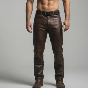 May include: Brown leather trousers with a matching belt. The trousers have a classic five-pocket design and a straight leg. The leather appears soft and has a slight sheen. The belt has a silver buckle.