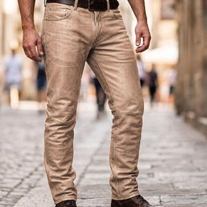 May include: Beige trousers with a brown leather belt and brown leather boots. The trousers have a textured finish and a classic five-pocket design. The belt has a silver buckle. The boots are lace-up style.
