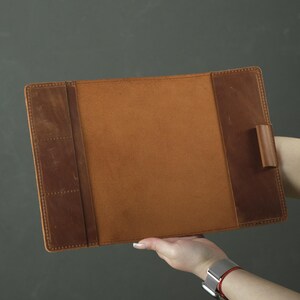 May include: A rectangular brown leather document holder featuring a smooth central panel, a left-side section with three vertical slots for cards or small items, and a single leather pen loop attached to the right-side interior panel.