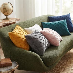 Può includere: Una collezione di sei cuscini quadrati nei colori giallo, bianco, grigio, rosa, verde acqua e blu navy. Ogni cuscino presenta un motivo a rombi trapuntato con linee cucite sulla superficie, creando un design geometrico a griglia.