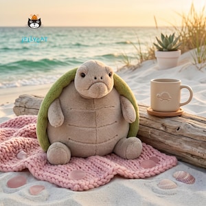 Puede incluir: Un peluche de tortuga con caparazón verde y cuerpo beige descansa sobre una manta rosa tejida en una playa de arena. Una taza beige con diseño de tortuga y un posavasos de madera están cerca. El logotipo de Jellycat es visible.