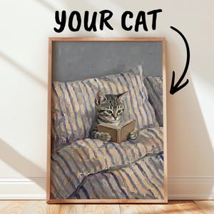 以下が含まれることがあります： ストライプ柄の枕の上で小さな本を読んでいるトラ猫の額入り絵画。フレームの上部には「YOUR CAT」という文字と、猫を指す矢印が描かれている。アートワークには目に見える筆致が施されている。