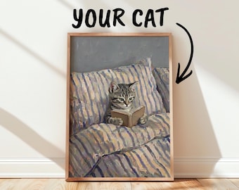 May include: A framed painting of a tabby cat reading a small book while resting on a striped pillow. Above the frame, the text reads YOUR CAT with an arrow pointing down toward the cat in the painting. The artwork features visible brushstrokes.
