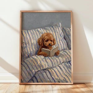 Pode incluir: Uma impressão de pintura a óleo emoldurada apresentando um cão castanho de pelo encaracolado sentado na cama. O cão segura um livro aberto com as patas, apoiado contra uma almofada grande e fofa com riscas verticais azuis e brancas.