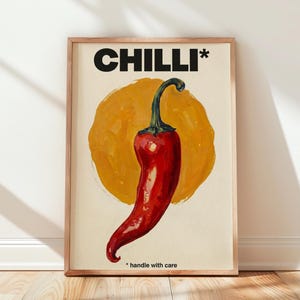 May include: A framed wall art print featuring a vibrant red chili pepper centered over a textured yellow circular brushstroke. The text CHILLI* appears in bold black letters at the top, with the phrase *handle with care printed at the bottom.