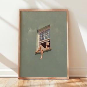 May include: A framed art print featuring a painting of a person sitting on a window ledge of a sage green wall, reading an open book. The window has a white frame with multiple panes. The person is wearing light-colored clothing and is barefoot.